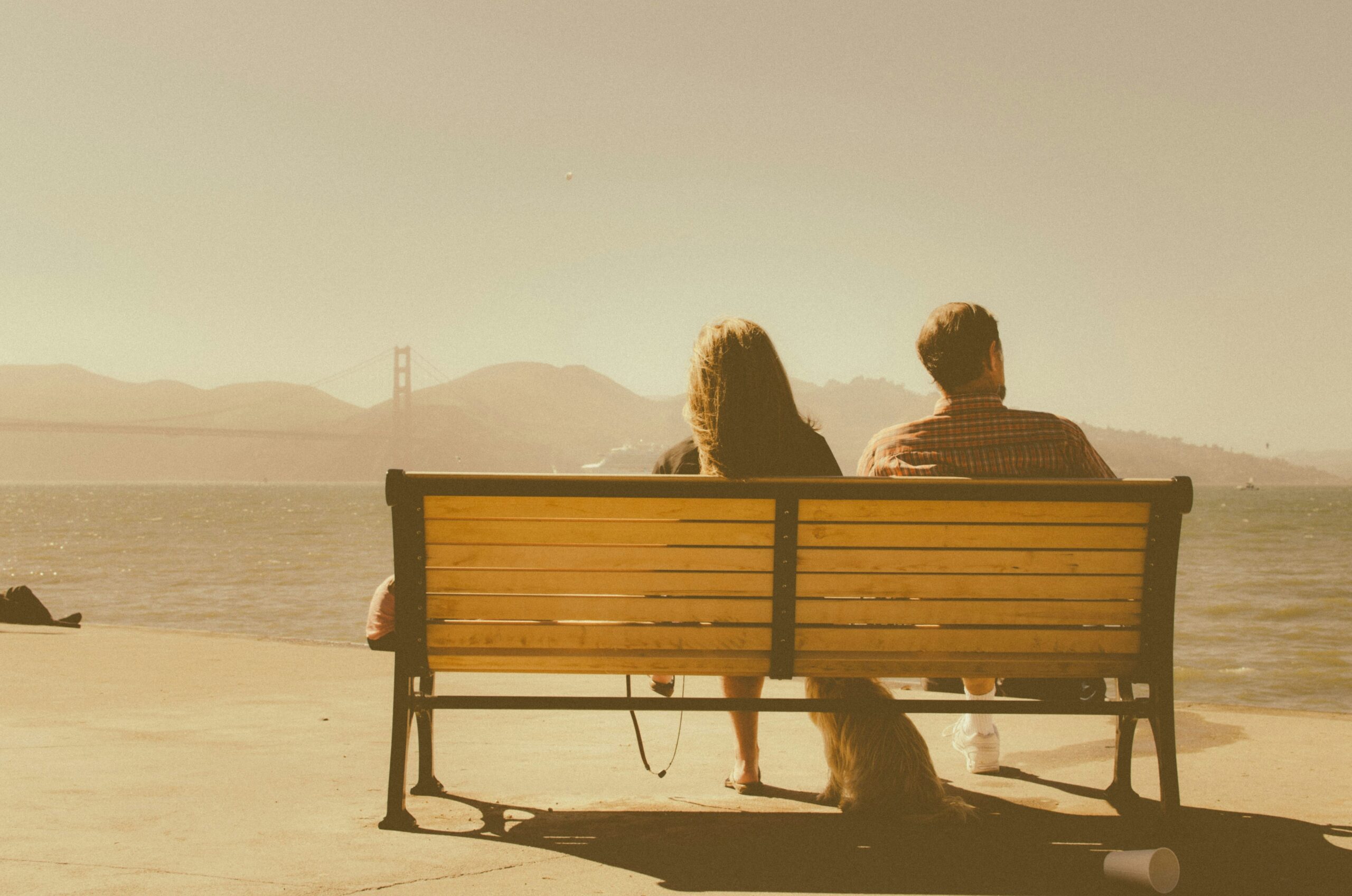 couple sitting on bench overlooking ocean and bridge