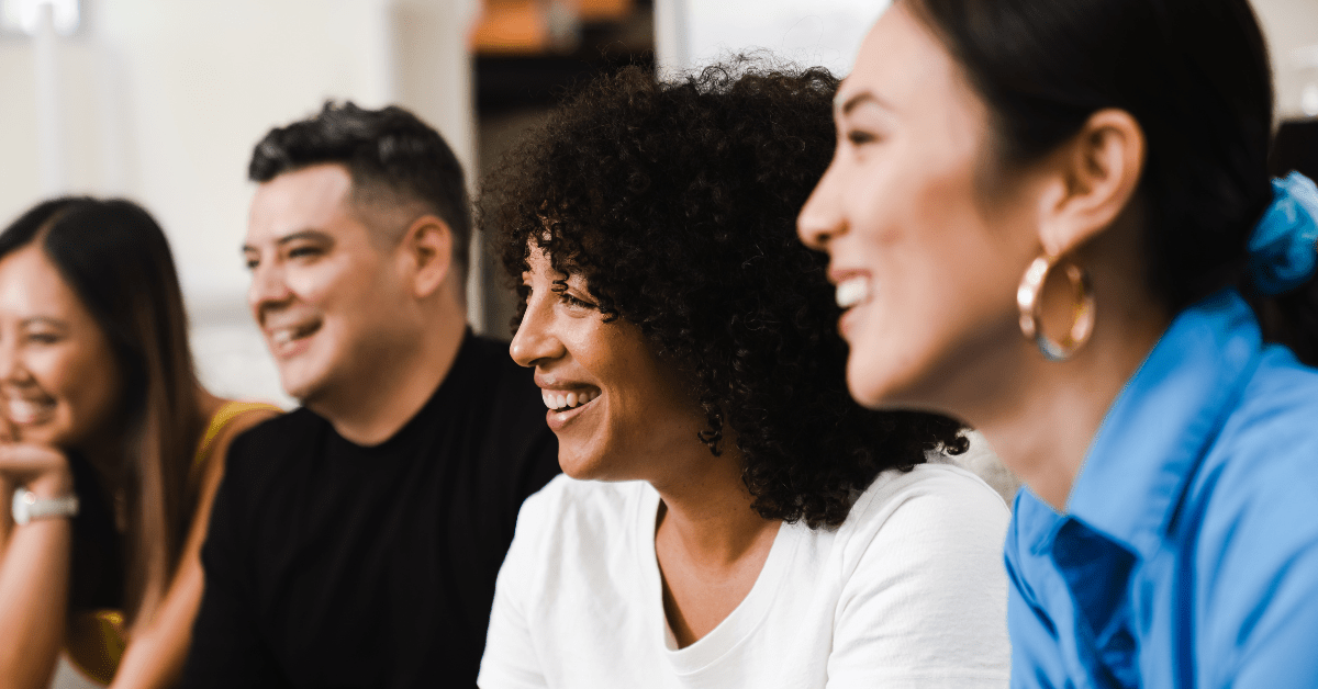Four people of different backgrounds smiling and listening together in a collaborative meeting.
