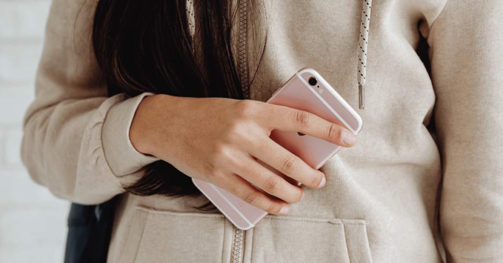 Person holding a smartphone in their hand while wearing a beige hoodie