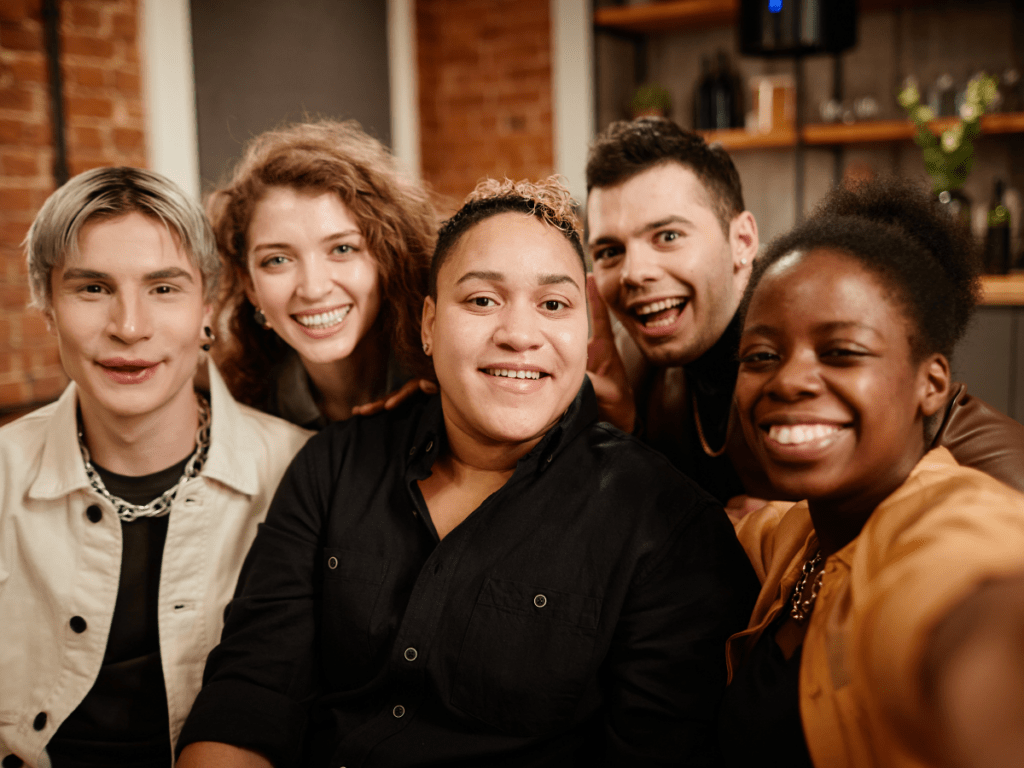 Group of queer friends smiling together while taking a selfie during a social gathering indoors promoting LGBTQ+ health