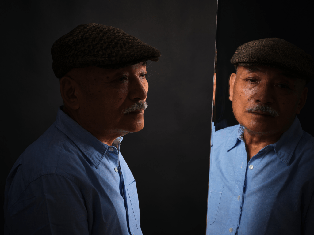 Older man looking at his reflection in a mirror, captured in soft, low light