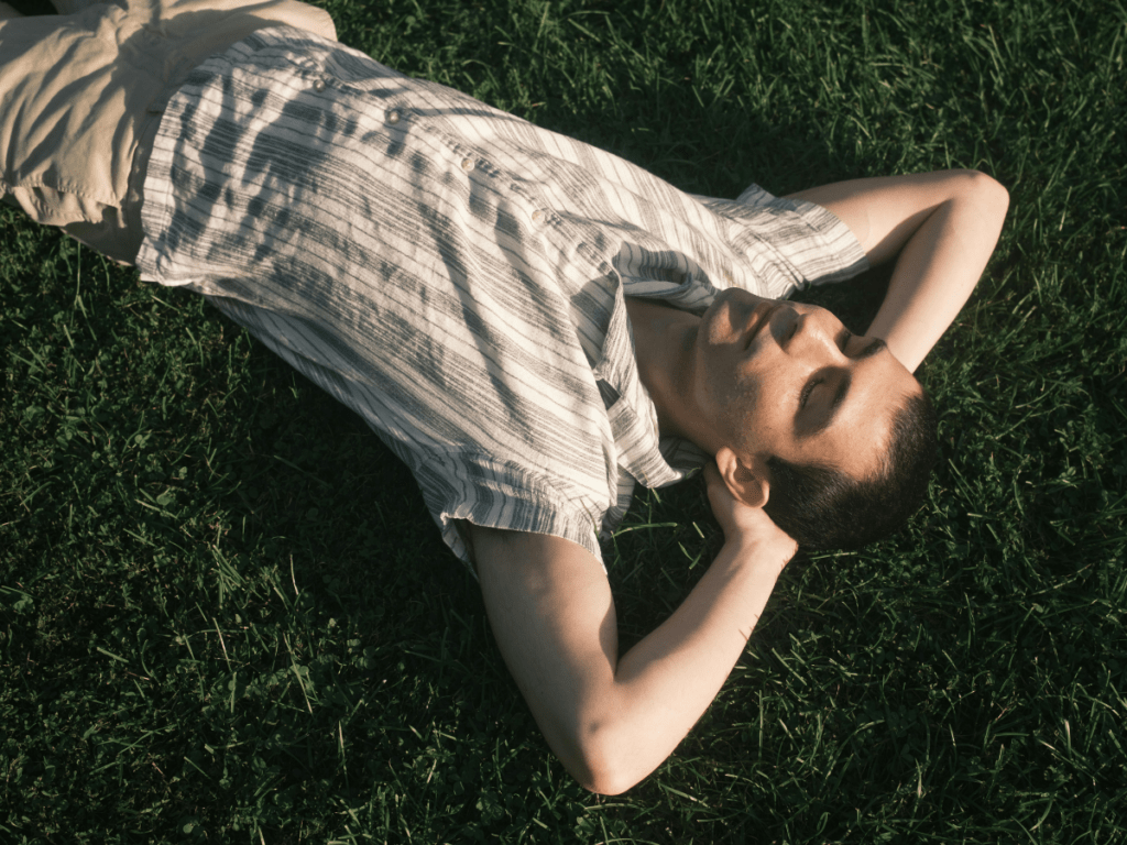 Person lying on grass with hands behind head, eyes closed in a calm, restful moment outdoors