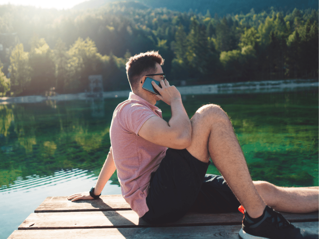 man taking a phone call on a doc at a small lake