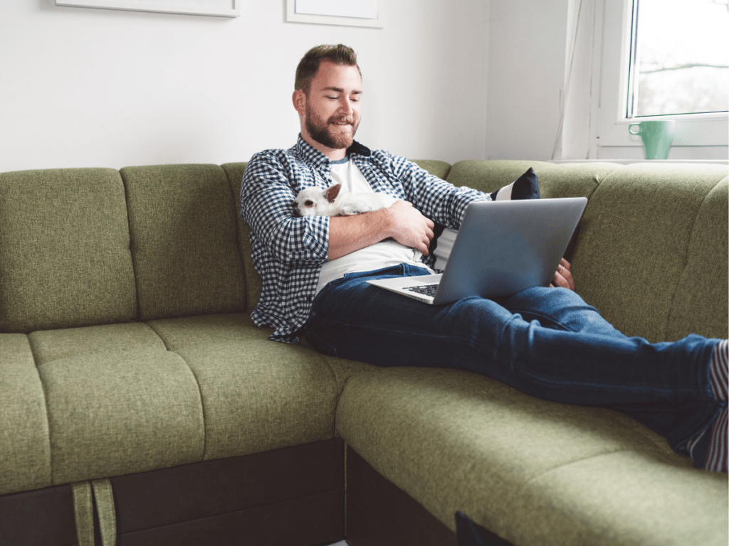 man sitting on green couch with small dog and laptop on his lap