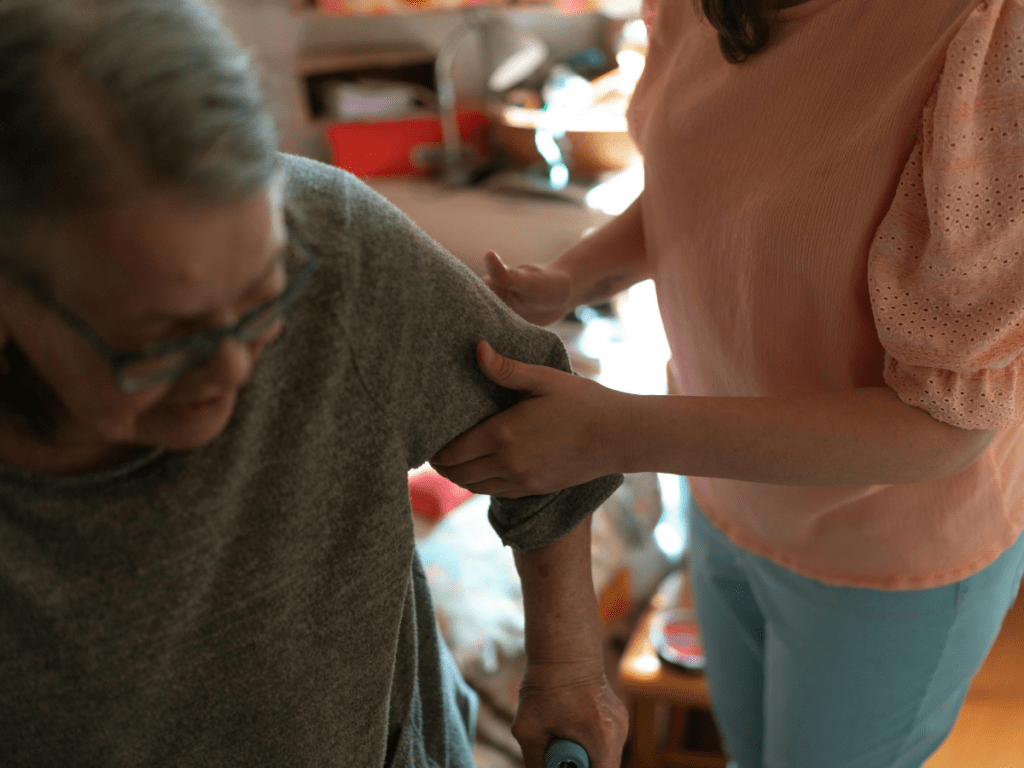 Adult family member helping an older adult stand and walk inside the home