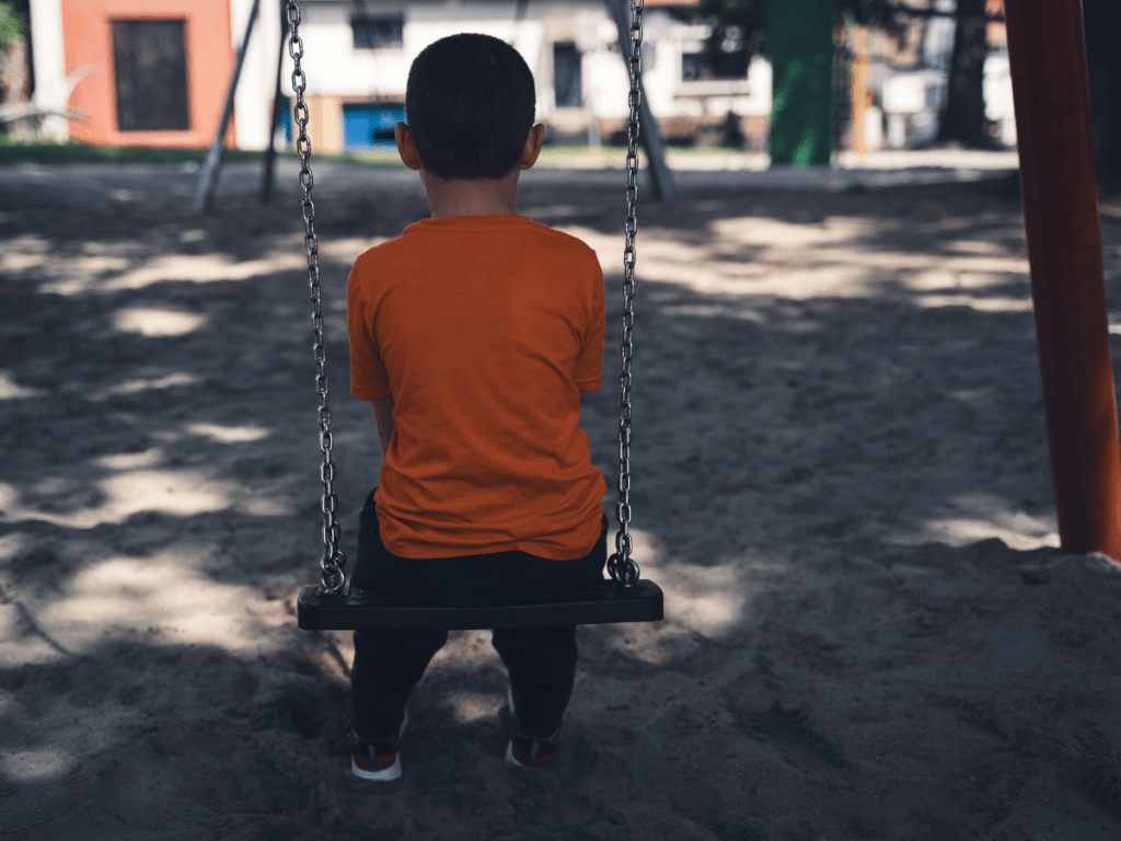 Child sitting alone on a playground swing viewed from behind