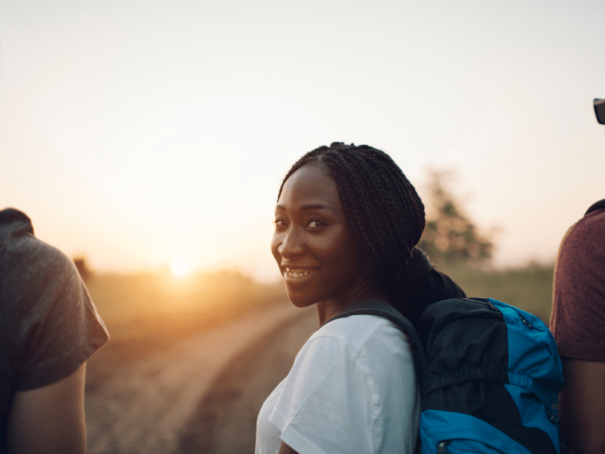 Backpacking woman looking back at camera smiling at sunset on a trail