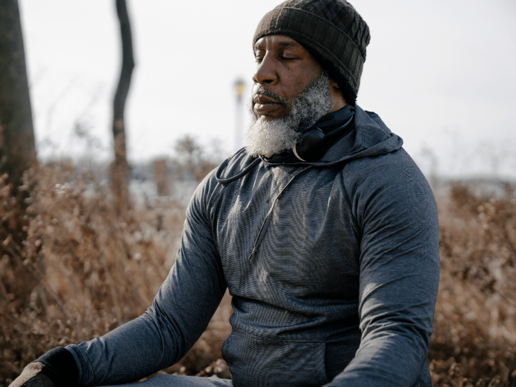 Older man wearing a beaning meditating outdoors