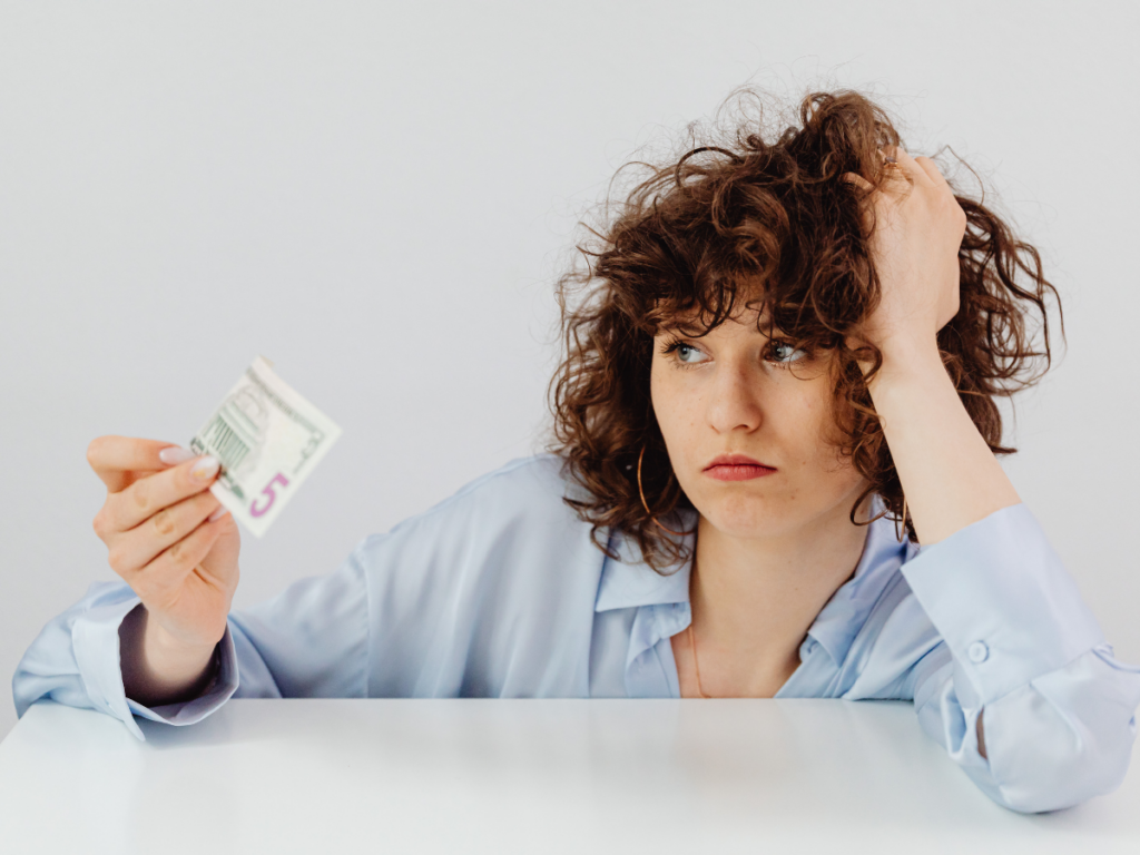 lady at a white desk holding five dollars and looking upset